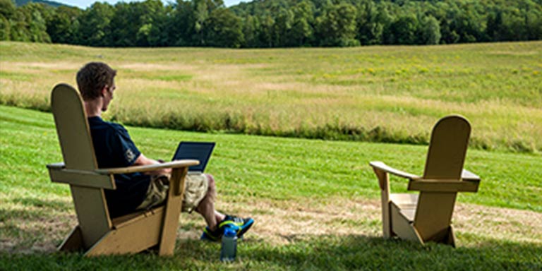 young man sitting in a chair with a laptop looking out to a field