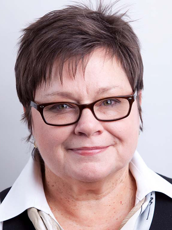 A headshot of Professor Kathy Smith, who wears a dark shirt with a white collar and dark, rectangular-frame glasses.