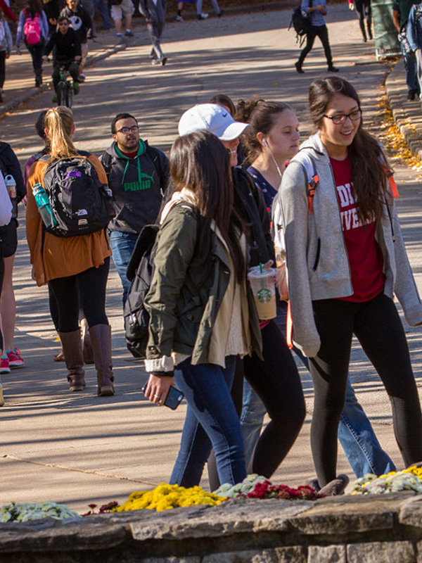 Groups of students walk to or from class near Ballantine Hall, with autumn leaves on the bending street in the background.